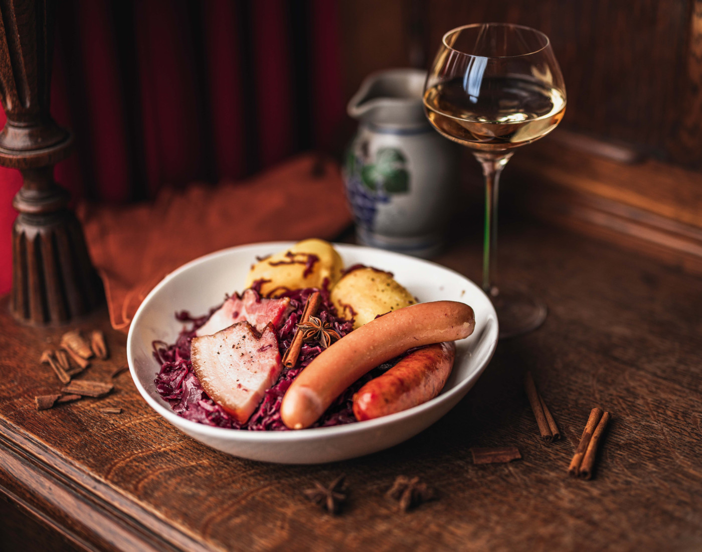 Rotes Sauerkraut mit Fleisch und Würstchen serviert auf einem Teller mit einem Glas Wein in rustikaler Umgebung