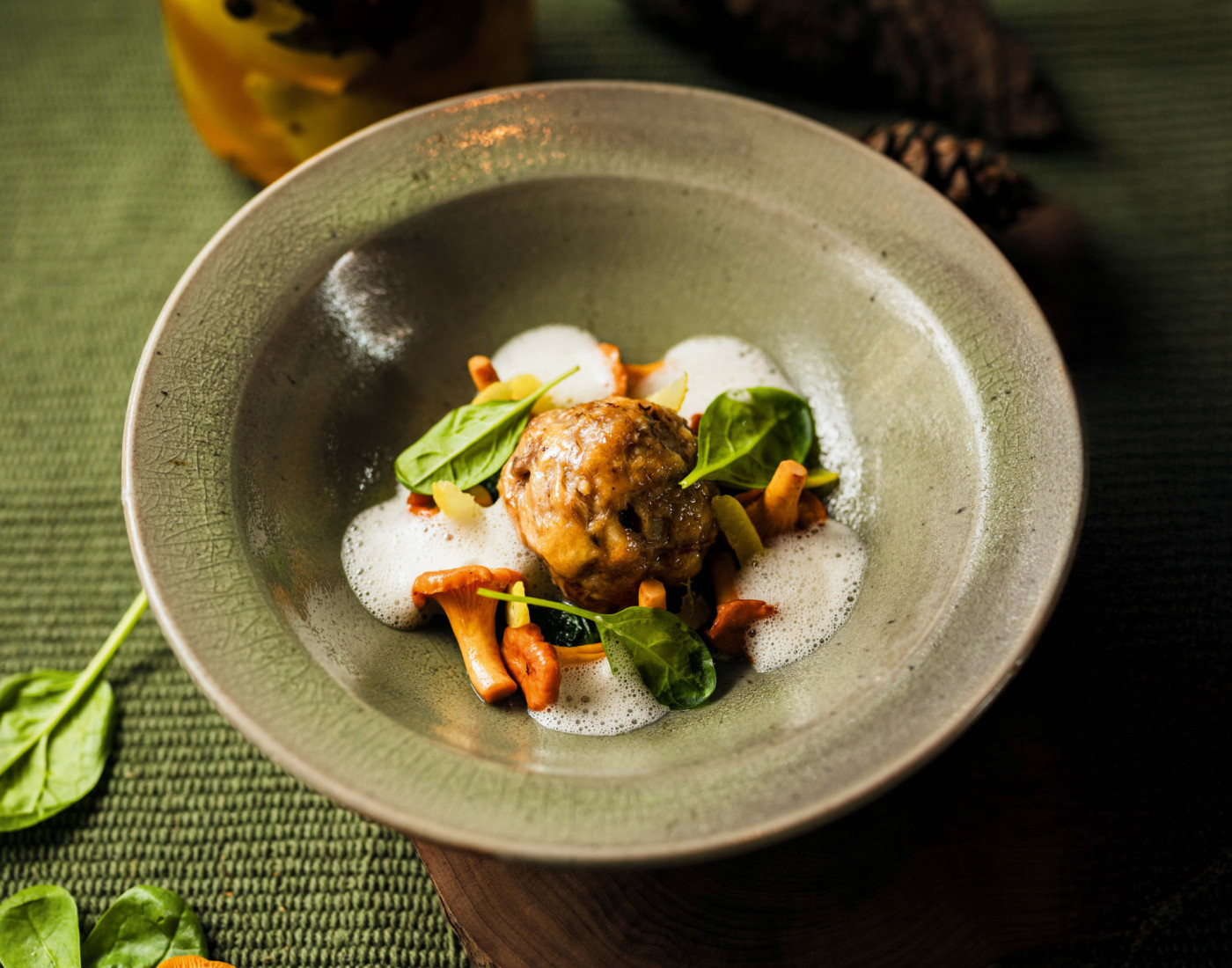 Semmelknödel mit Pfifferlingen, Salzzitronen und Spinat serviert auf grünem Teller auf grünem herbstlich dekoriertem Untergrund