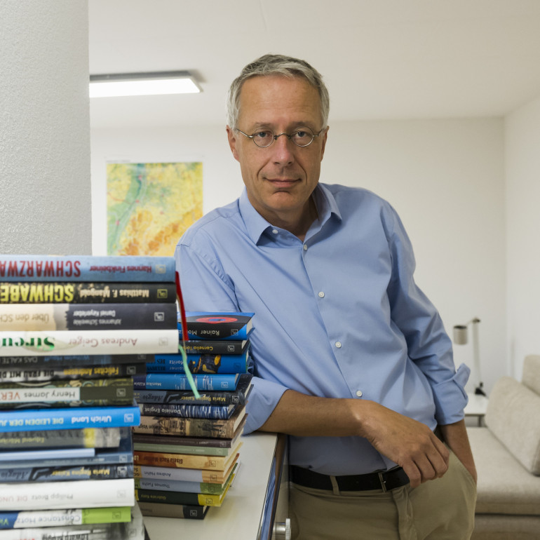 Der Freiburger Verleger steht hinter einem Stapel Bücher und schaut frontal in die Kamera