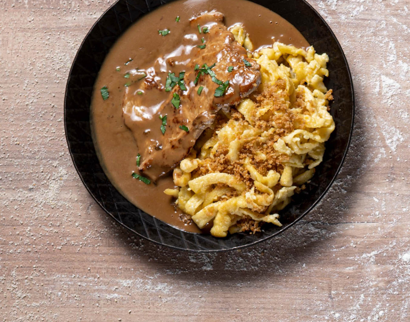 Ein Rahmschnitzel wurde neben Spätzle in einer Gusseisen-Pfanne angerichtet.
