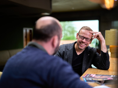 Ulf Tietge im Interviewgespräch an einem Tresen, lachend im Gespräch mit einem Gegenüber