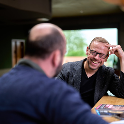 Ulf Tietge im Interviewgespräch an einem Tresen, lachend im Gespräch mit einem Gegenüber