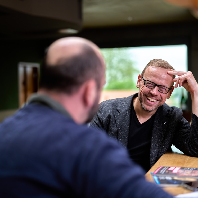 Ulf Tietge im Interviewgespräch an einem Tresen, lachend im Gespräch mit einem Gegenüber