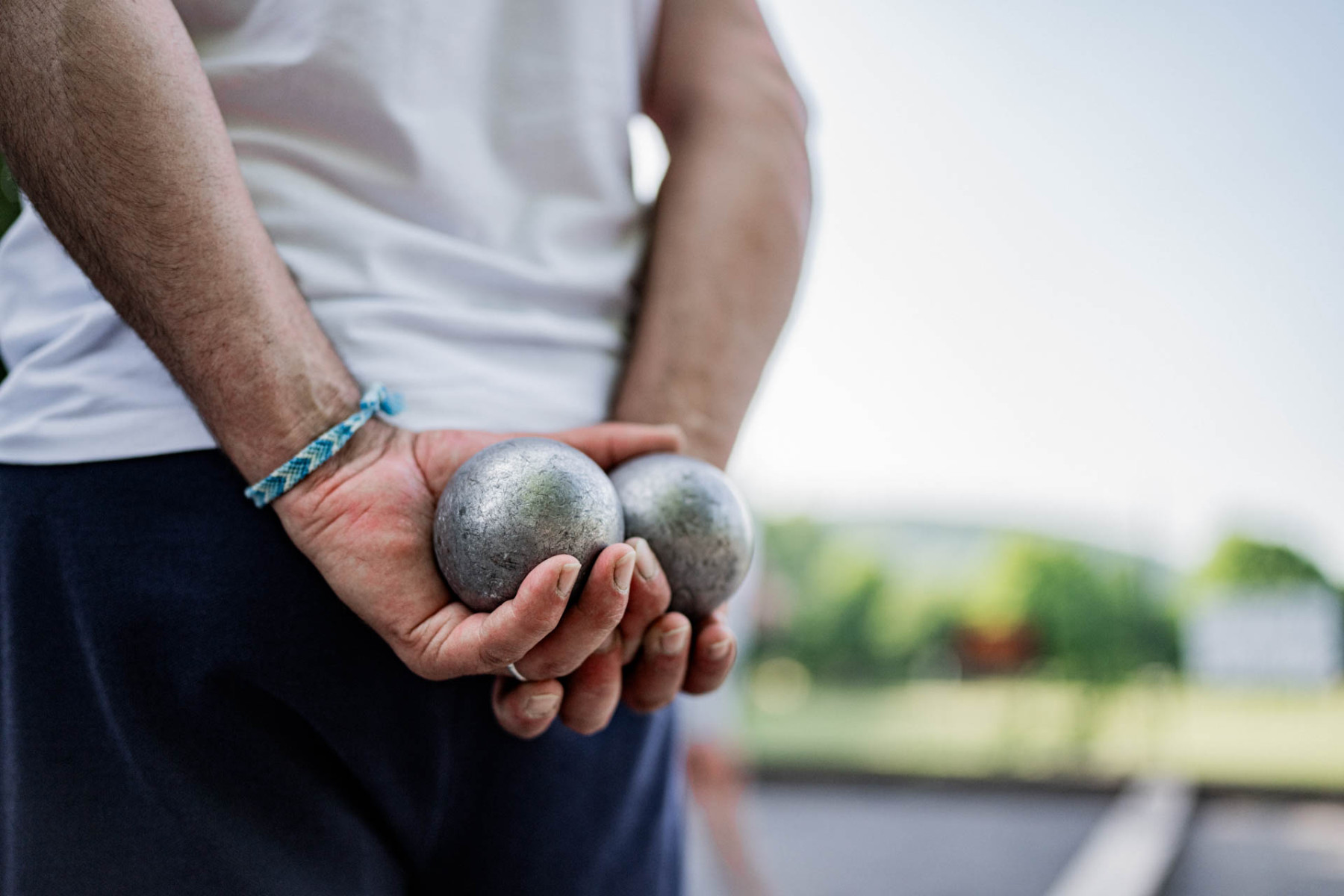 Zwei Hände halten zwei silberne Boule-Kugeln hinter dem Rücken versteckt.