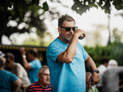 Ein Mann in einem hellblauen T-Shirt holt aus, um eine Boule-Kugel zu werfen.