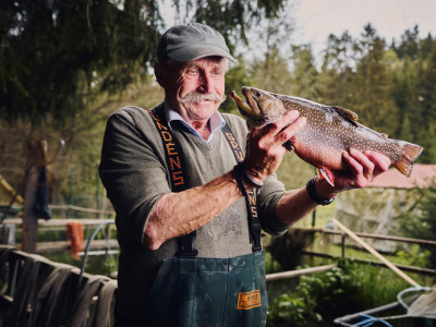 Ein Forellenzüchter hält einen Fisch in die Höhe und lächelt.