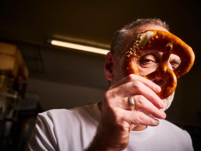 Ein Mann hält eine Brezel vor sein Gesicht und blickt verschmitzt durch eines der Löcher.