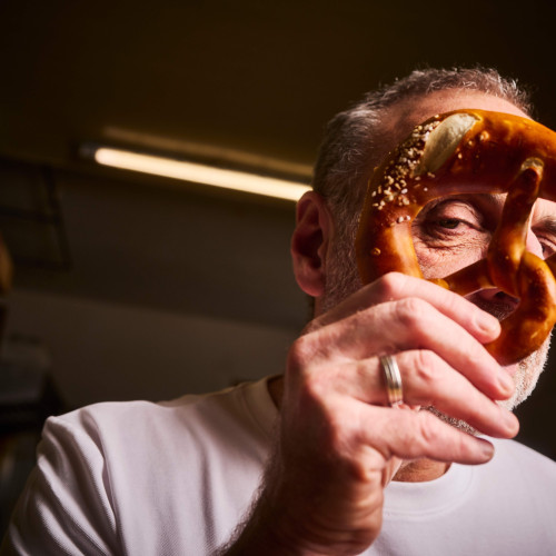 Ein Mann hält eine Brezel vor sein Gesicht und blickt verschmitzt durch eines der Löcher.