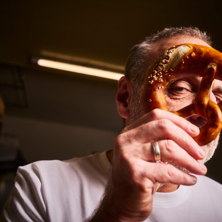 Ein Mann hält eine Brezel vor sein Gesicht und blickt verschmitzt durch eines der Löcher.