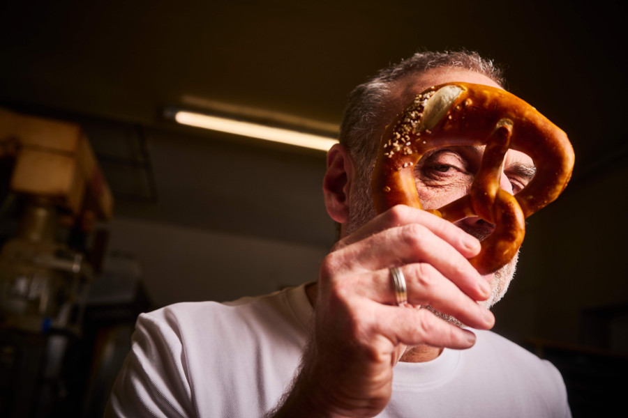 Ein Mann hält eine Brezel vor sein Gesicht und blickt verschmitzt durch eines der Löcher.