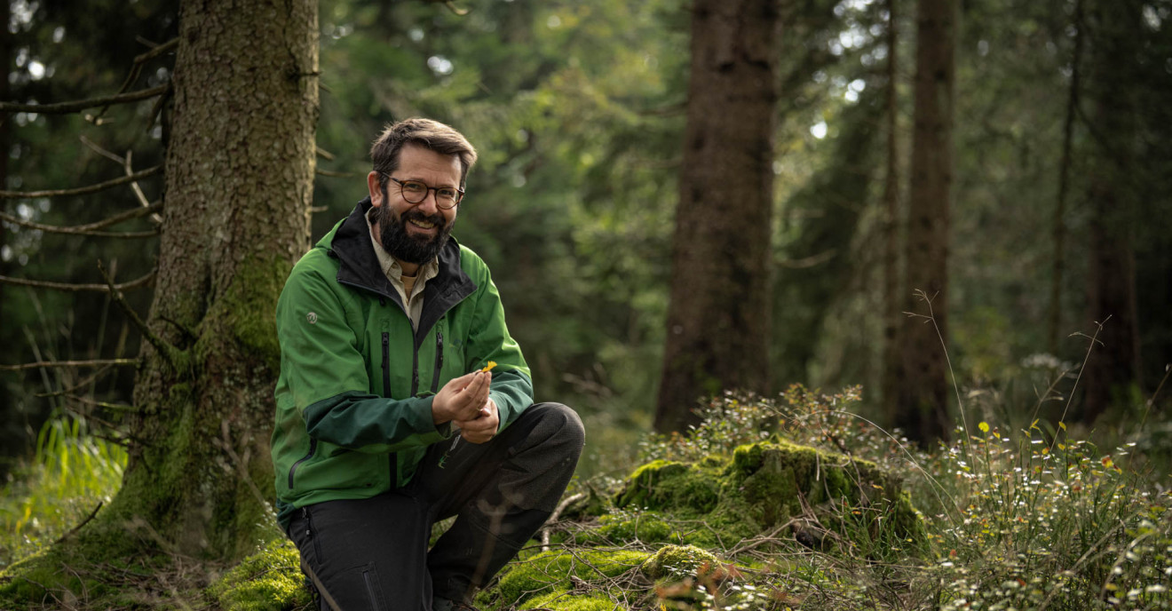 Pilzforscher Flavius Popa kniet auf dem Waldboden und präsentiert einen Pilz.