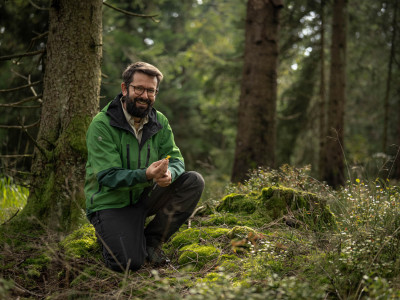 Pilzforscher Flavius Popa kniet auf dem Waldboden und präsentiert einen Pilz.