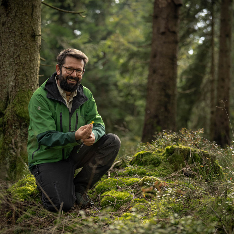 Pilzforscher Flavius Popa kniet auf dem Waldboden und präsentiert einen Pilz.
