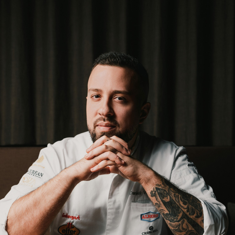 Ein Koch mit Tattoos sitzt an einem Esstisch 