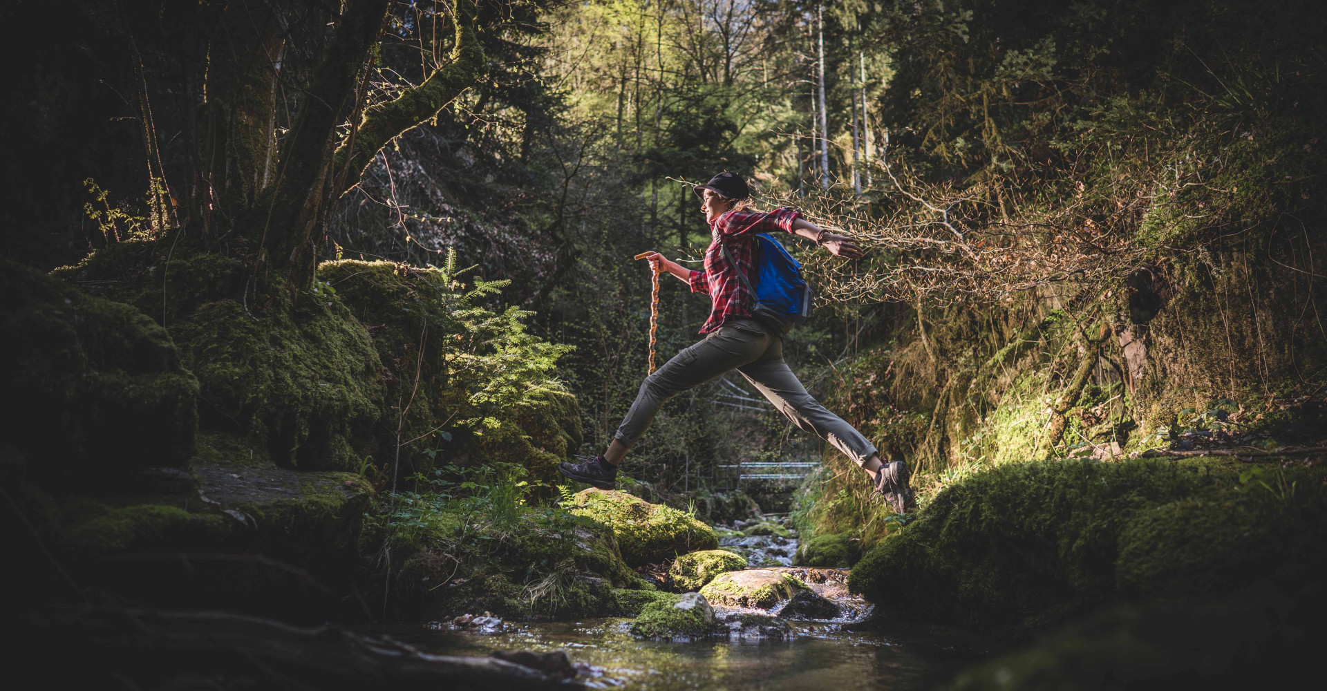 Eine Wanderin springt über einen Bach