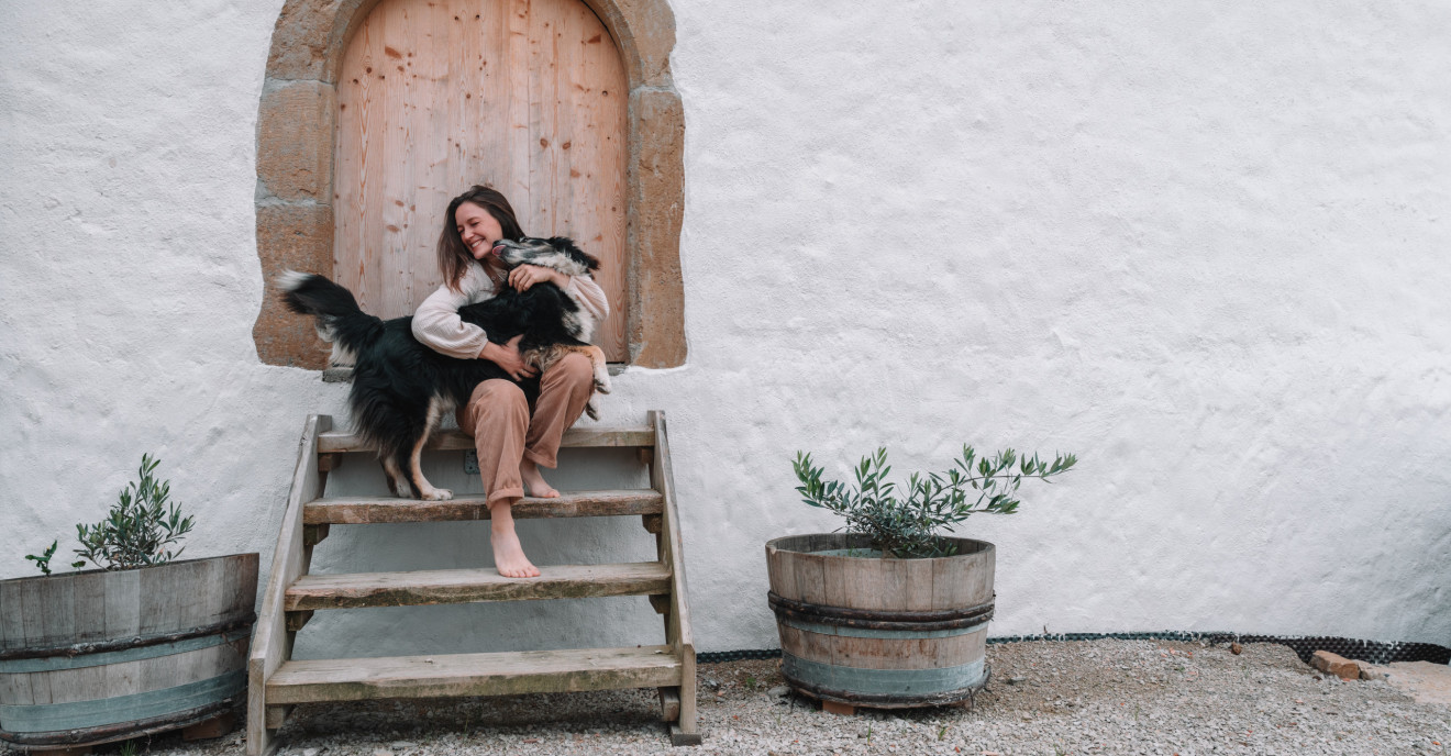 Eine junge Frau sitzt mit ihrem Hund vor einem Hoftor
