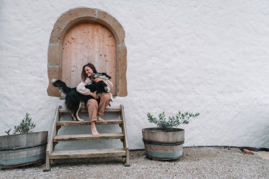 Eine junge Frau sitzt mit ihrem Hund vor einem Hoftor