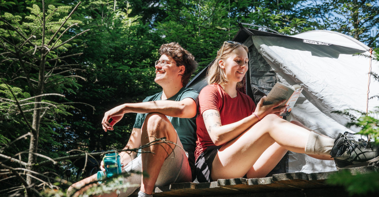 Ein junges Paar sitzt im Schwarzwald vor einem aufgebauten Zelt. 