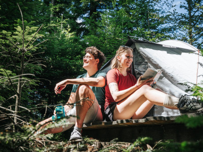 Ein junges Paar sitzt im Schwarzwald vor einem aufgebauten Zelt. 