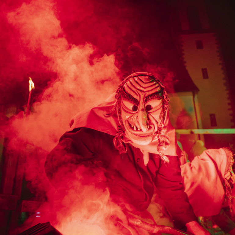 Eine Hexe tanzt zur Fastnacht im Dunkeln auf einer rot beleuchteten Bühne