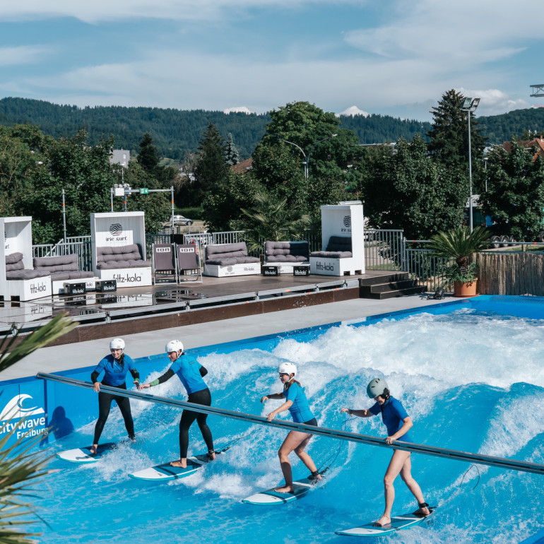 Vier Personen surfen auf einer künstlichen Welle